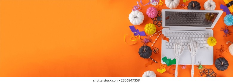 Funny Halloween bright yellow composition. White laptop with typing skeleton hands, Halloween decor colorful holiday accessories - spiders, cobwebs, pumpkins, bats, top view copy space banner - Shutterstock ID 2356847359