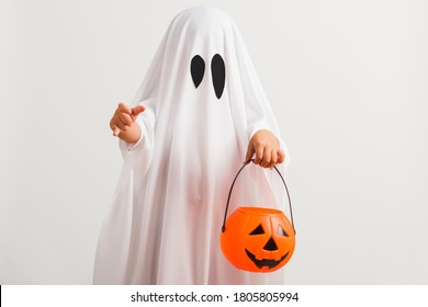 Funny Halloween Kid Concept, Little Cute Child With White Dressed Costume Halloween Ghost Scary He Holding Orange Pumpkin Ghost On Hand, Studio Shot Isolated On White Background