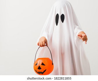 Funny Halloween Kid Concept, Little Cute Child With White Dressed Costume Halloween Ghost Scary He Holding Orange Pumpkin Ghost On Hand, Studio Shot Isolated On White Background