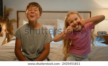 Funny happy Caucasian children kids boy girl brother sister siblings son daughter friends teasing camera at home grimacing playing together fooling around making faces showing tongue joking in bedroom