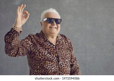 Funny Happy Cheerful Rich Fat Chubby Old Man In Leopard Patterned Shirt, Gold Chain Bracelet And Sunglasses Doing Okay, OK, Okey Dokey, Alright, No Problem Sign Standing On Gray Studio Background