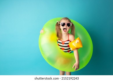 Funny happy child in bright swimsuit and sun glasses smiling and holding a swimming ring on colored background. Summer and vacation concept.