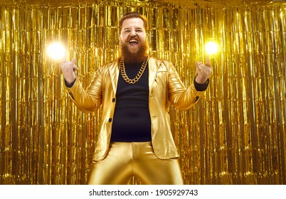 Funny Happy Crazy Uninhibited Bearded Chubby Man In Funky Golden Suit And Extravagant Gold Chain Having Fun At Disco Club Party, Celebrating Success, Screaming For Joy And Doing Horn Sign Hand Gesture