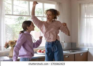 Funny Happy Family Young Adult Mom And Teen Daughter Enjoying Dancing, Singing, Jumping In Kitchen Cooking Together. Cheerful Mother Having Fun With Teenage Child Girl Preparing Healthy Meal At Home.