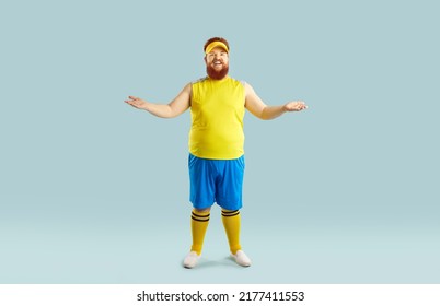 Funny Happy Fat Young Man In Yellow Top And Blue Shorts Standing Isolated On Blue Background, Smiling And Spreading Arms In Welcoming Gesture Inviting You To Join Sports Gym Workout For Losing Weight