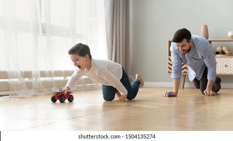 Funny Happy Male Family Young Adult Dad And Cute Excited Little Kid Son Pretending Racing On Warm Wooden Floor At Home, Father Having Fun Chasing Small Preschool Child Boy Playing Cars Together