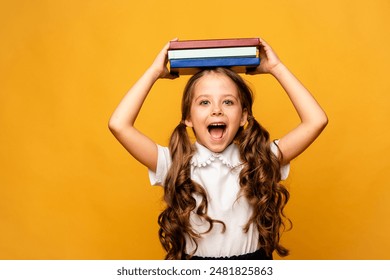 Funny happy Preschool Child girl with Book on Head and Bag on Yellow Background, Copy Space. Happy Smiling Kid Go Back to School, Kindergarten. Success, Motivation, Winner Genius - Powered by Shutterstock