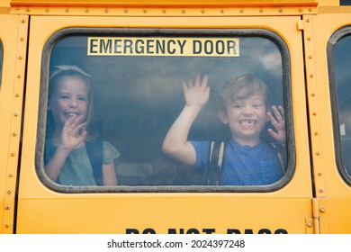 Funny happy smiling boy and girl kids students looking out of school yellow bus window. Waving saying goodbye to parents before school day start. Classmates meeting after summer break. 