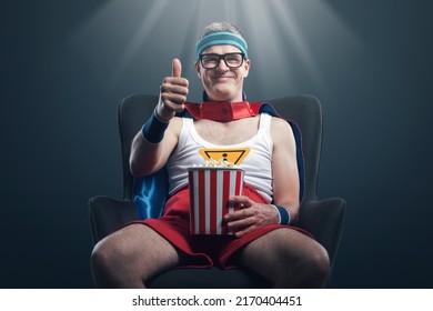Funny happy superhero watching movies and eating popcorn, he likes the movie and gives a thumbs up