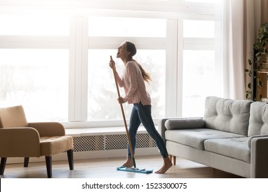 Funny happy young woman holding mop microphone singing song in modern living room interior with big window, carefree active funky girl having fun cleaning floor at home enjoying housework alone - Powered by Shutterstock