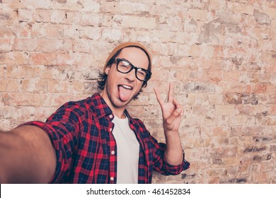 funny hipster making selfie photo and showing tongue  near brick wall
