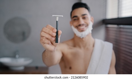 Funny Hispanic Indian Arab Naked Man 30s Bearded Guy Standing In Bathroom At Home With White Soapy Foam On Beard Shaving Gel Smiling Showing Razor Looking At Camera Getting Ready To Shave Facial Care