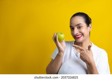 A Funny Hispanic Woman Pointing To A Green Apple Isolated On A Yellow Background