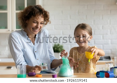 Funny home lab. Excited emotional parent mother daughter kid watch result of self made chemical test at home kitchen. Laughing young female babysitter help junior girl carry out scientific experiment Stock photo © 