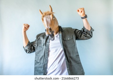 Funny horse head on human body on a green shirt on blue background, fists up, strong and win symbol . Clip art, negative space.