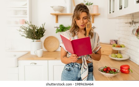 Hübsche Hausfrau, die sich die Rezepte in Kochbüchern ansieht, die Gemüsesalat zubereiten und in der hellen Küche zu Hause kochen. Diät gesunden Lebensstil Konzept.