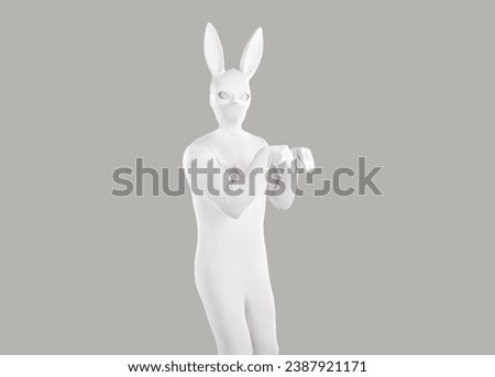 Funny human model pretends to be a bunny. Man disguised in a white skin tight spandex bodysuit costume and long eared playboy rabbit mask hopping like a rabbit on a gray color studio background