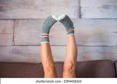 Funny Image For Feet With Nice And Funny Socks Colored. Cacuasian Woman Up And Down Side On The Sofa. Cener Part Of Body Scene At Home. Like Wood Background