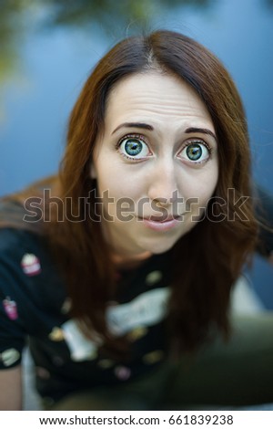 Funny image of a girl with big blue eyes. Young pity woman with big eyes and grimace on face.
