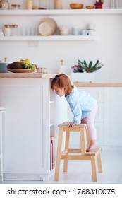 Funny Infant Baby Girl Climbing A Step Stool At The Cozy Kitchen At Home