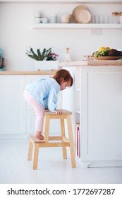 Funny Infant Baby Girl Climbing A Step Stool At The Cozy Kitchen At Home