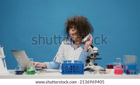 Funny insane female scientist looking at test tubes on desk, acting crazy and foolish in front of camera. Mad amusing chemist being messy after smoke explosion, doing silly goofy expressions.
