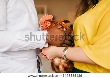 Funny interracial couple holding chicken in hands in home interior. 