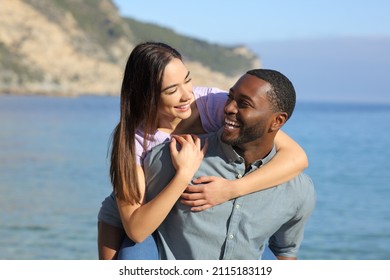 Funny interracial couple joking on piggyback on the beach on summer - Shutterstock ID 2115183119