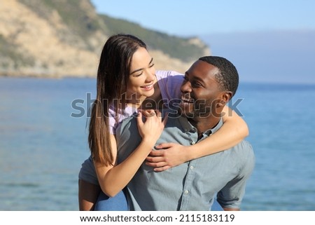 Funny interracial couple joking on piggyback on the beach on summer