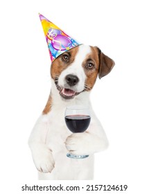 Funny Jack russell terrier puppy wearing party cap holds glass of red wine. isolated on white background