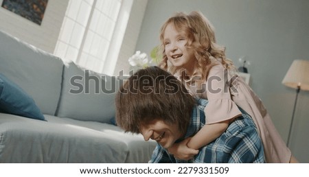 Funny joyful little caucasian girl having a piggy back ride on her father while he is doing push ups, spending time at home together - real people, family home  Foto stock © 