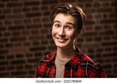 A funny joyful teenage boy in youth casual clothes stands against the background of a brick wall looking very excitedly at the camera. Youth emotions. 