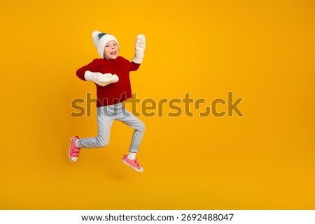 Funny jumpy kid in red sweater leaps against bright yellow background creating playful festive holiday style image
