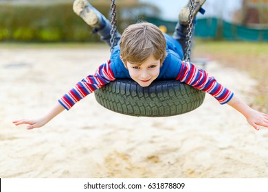 Funny Kid Boy Having Fun With Chain Swing On Outdoor Playground. Child Swinging On Warm Sunny Spring Or Autumn Day. Active Leisure With Kids. Boy Wearing Casual Colorful School Kid Clothes