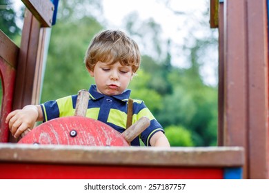 Funny Kid Boy Pretends Driving An Imaginary Car On Children Playground, Outdoors. On Warm Summer Day.