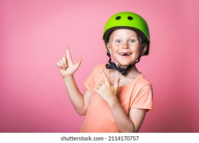 Funny Kid In Bright Green Helmet Pointing Up With Finger Isolated On Pink Background. School Boy With Missing Front Tooth. Happy School Boy Smiling 