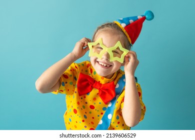 Funny Kid Clown Against Blue Background. Happy Child Playing With Festive Decor. Birthday And 1 April Fool's Day Concept.