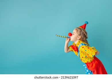 Funny kid clown against blue background. Happy child playing with festive decor. Birthday and 1 April Fool's day concept.