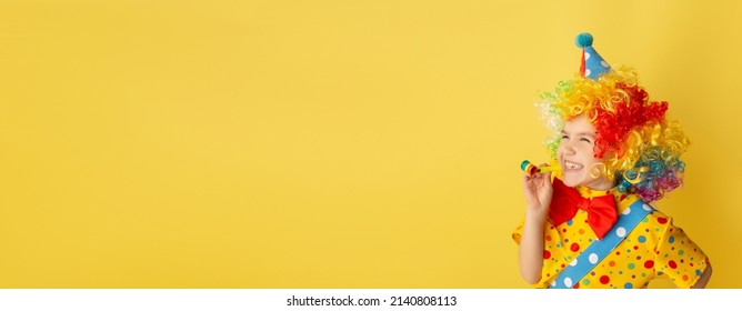 Funny kid clown against yellow background. Happy child playing with festive decor. Birthday and 1 April Fool's day concept.