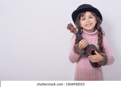 Funny kid girl with guitar, ukulele guitar. Fashionable country girl playing music. 