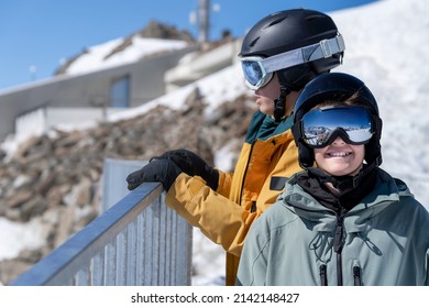 A funny kid in ski gear looks at the camera with a smile while another looks over the fence.Ski vacation concept