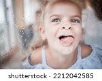 Funny, kid and tongue on window portrait with goofy and enthusiastic face pressed on surface. Young, happy and crazy girl child enjoying playful lick on glass with rain droplets closeup.