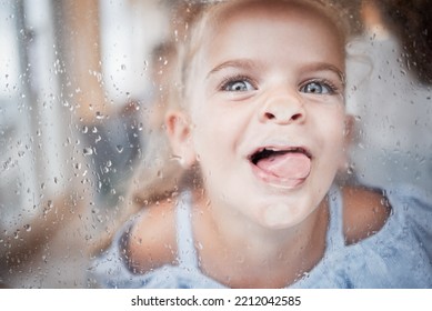 Divertido, chico y lengua en la ventana retrato con cara tonta y entusiasta sobre la superficie. Niña joven, feliz y loca que disfruta de lecha juguetona en el vaso con gotas de lluvia cerradas.