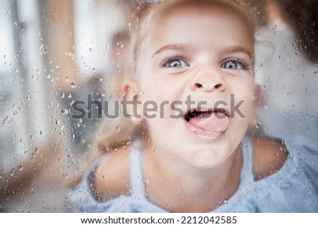 Funny, kid and tongue on window portrait with goofy and enthusiastic face pressed on surface. Young, happy and crazy girl child enjoying playful lick on glass with rain droplets closeup.