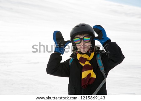 Funny kid with in warm clothes and protection equipment taunts. White snow background.