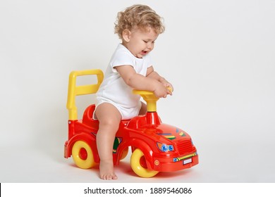 Funny Kid Wearing White Bodysuit Posing Barefoot Isolated Over White Background, Being Upset, Starts Crying, Playing With Red Toy Car, Child Driving Toy Vehicle.