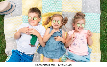 Funny Kids Fooling Around At Summer Camp On Vacation. Children Try On A Cucumber Mask. Unschooling Concept. Joyful Smiling Children Have Fun.