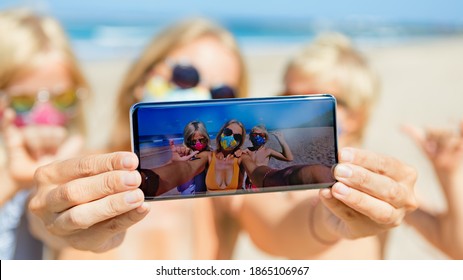 Funny kids with mother taking selfie photo by smartphone on tropical sea beach. Rule to wear face covering mask at public places due coronavirus COVID 19. Family holidays with children, summer travel. - Powered by Shutterstock