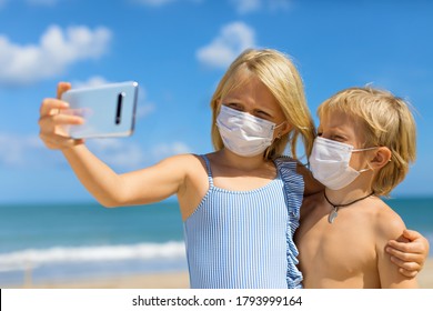 Funny Kids Taking Selfie Photo By Smartphone On Tropical Sea Beach. New Rules To Wear Cloth Face Covering Mask At Public Places Due Coronavirus COVID 19. Family Holidays With Children, Summer Travel.