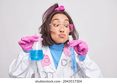Funny laboratory worker checks analysis holds glass beaker and tube conducts chemical research dressed in labcoat isolated over grey background studies new technology in science. Biotechnology